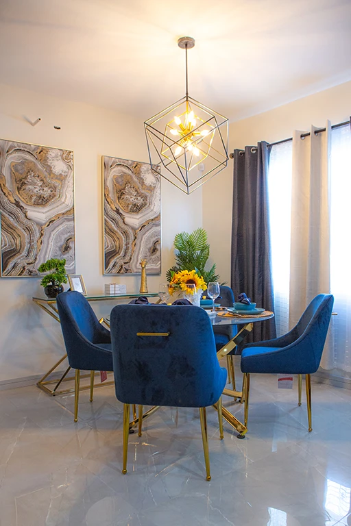 Comedor elegante con una mesa redonda de cristal y sillas acolchonadas en color azul con patas doradas.