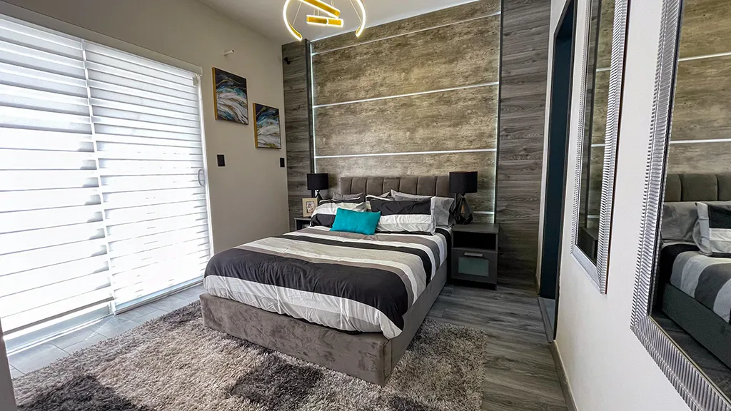 Dormitorio principal moderno con una cama matrimonial vestida con sábanas y colchas en tonos grises y blancos.