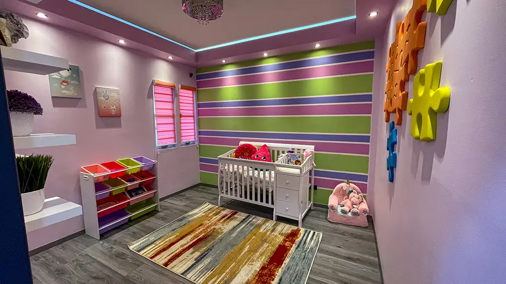 Habitación infantil decorada con paredes de colores vivos en tonos de rosa, verde y azul, con franjas horizontales.
