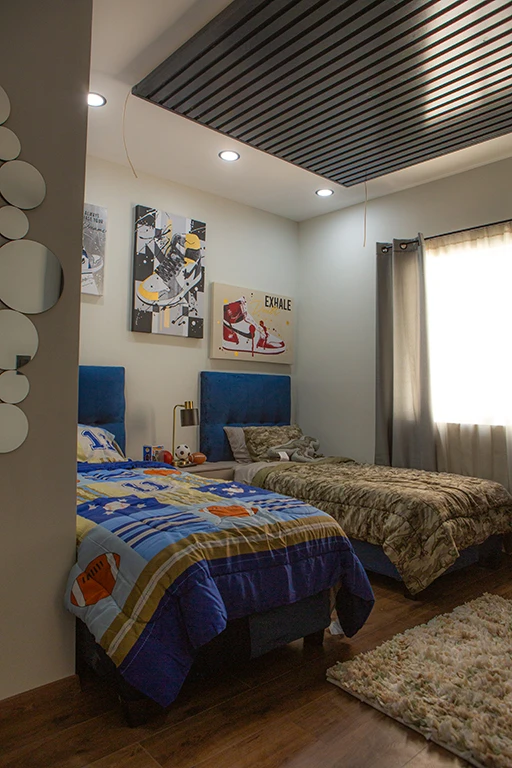 Dormitorio infantil con dos camas individuales, cada una con cabeceras tapizadas en azul.