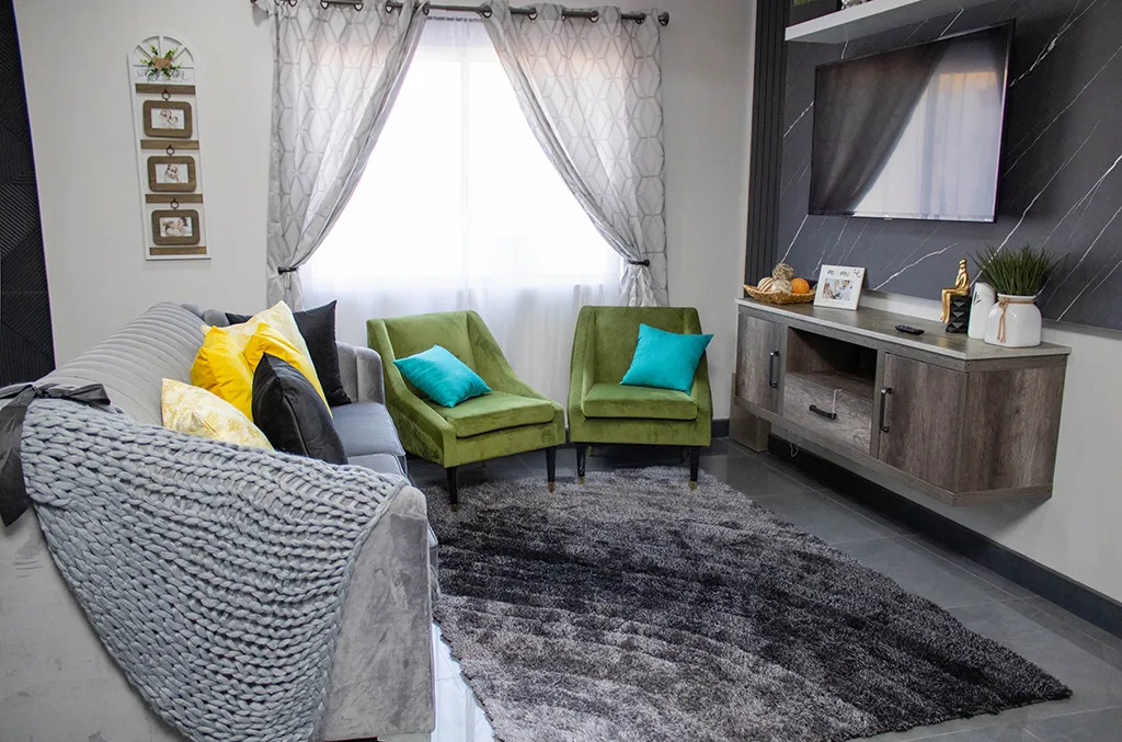 Sala de estar moderna con un sofá gris decorado con cojines amarillos y negros, junto a dos sillones verdes con cojines azules.